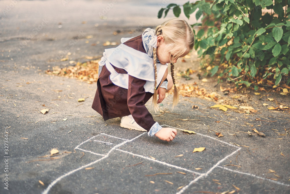 Fototapeta premium little girl draws with chalk on the pavement. schoolgirl plays in the yard. creativity concept.