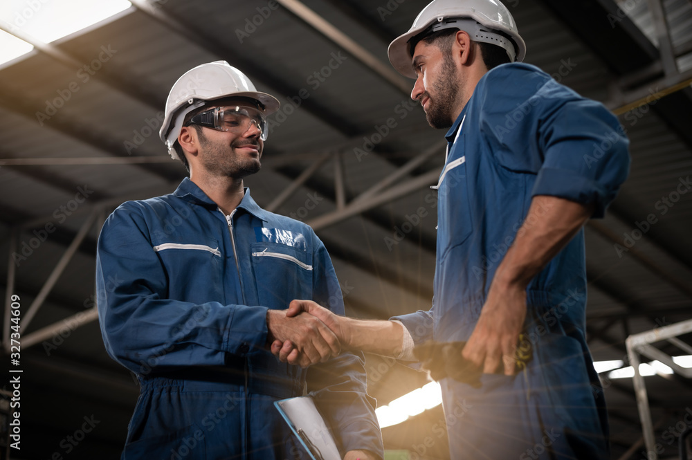 Technicians at the factory hand in hand to congratulate each other. They can reach an agreement of collaboration. They wear uniforms, safety helmets, and protective goggles. Technicians at the factory hand in hand to congratulate each other. They can reach an agreement of collaboration. They wear uniforms, safety helmets, and protective goggles.