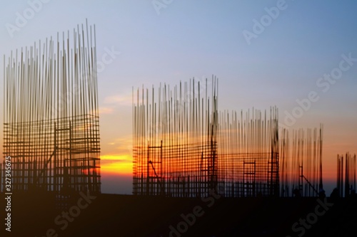 The construction of a rooftop high rise building, workers are tied with steel bars for concrete pouring, surveying the site and cranes are lifting or moving metal at the construction site. Pastel tone