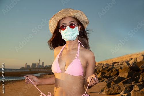 An senior Asian woman dressed in a pink swimsuit wears a straw hat and has a nose mask. Lantan Virus COVID-19 and PM2.5 protection. photo