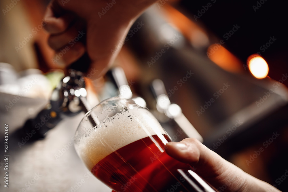 Closeup hand barman dark craft cold beer pour in glass from crane in pub
