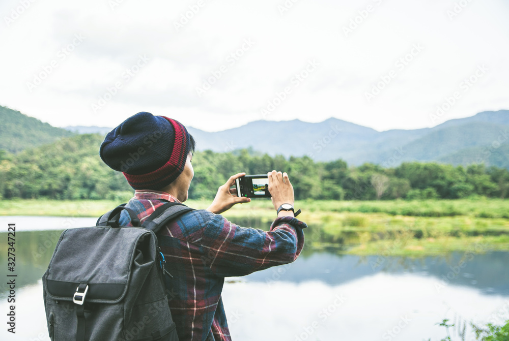 Standing back the Asian man using Camera smartphone Selfie taken of yourself connected to digital camera shooting photo Mountain river landscape. Traveling, Hiking concept. Standing back the Asian man using Camera smartphone Selfie taken of yourself connected to digital camera shooting photo Mountain river landscape. Traveling, Hiking concept.