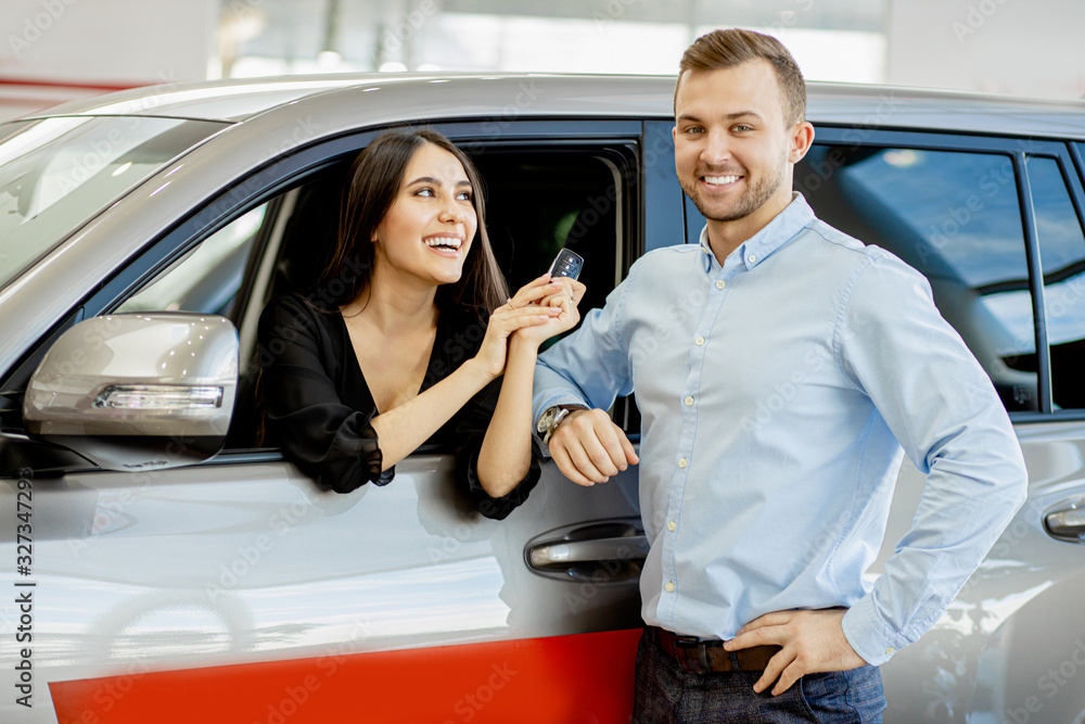 happy married caucasian couple with their new purchased car in dealership. young man and woman posing at camera with keys from their new auto happy married caucasian couple with their new purchased car in dealership. young man and woman posing at camera with keys from their new auto