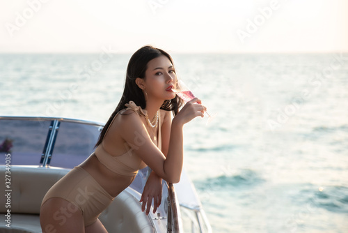 Sexy Asian Women in Bikini with Champagne Glass on her Private Yacht at Sunset.