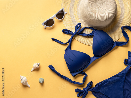 Top view of beach accessories. female bikini swimsuit, hat and sun glasses on a yellow background. copy space.