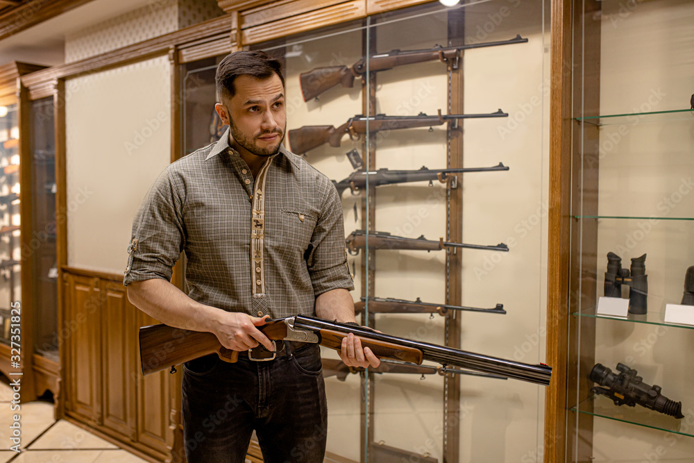 professional caucasian hunter looking for best rifle in guns store, he hold firearm in hands, want to make purchase