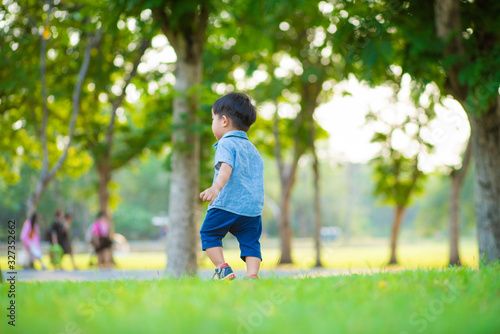 Adorable toddler boy walking on green grass city park sunset