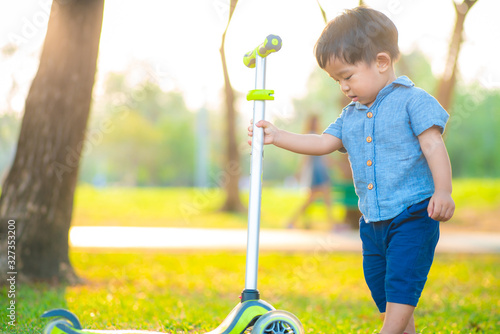 Little boy playing child scooter in city prak on green meadow photo