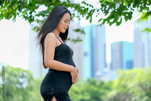 Free Download Pretty young pregnant woman stand in park or garden with high building as background. - GFXLoad