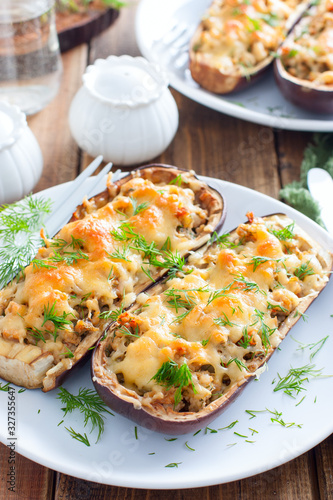 Baked stuffed eggplant with minced meat with cheese on a white plate on a wooden table, selective focus
