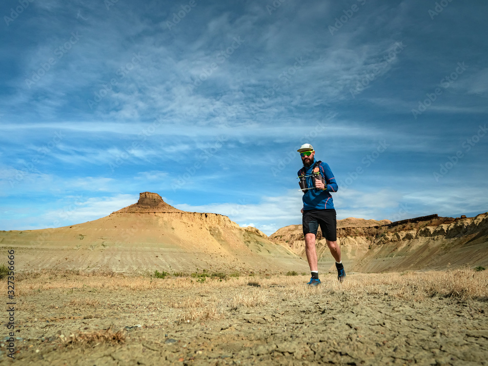 Runner athlete with backpack running on the wild trail at red mountains in the desert. The ledges of the Ustyurt plateau
