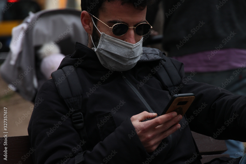 European young man looking at his smartphone with a medical mask on his face. A man in a protective mask is protected from the virus. European young man looking at his smartphone with a medical mask on his face. A man in a protective mask is protected from the virus.
