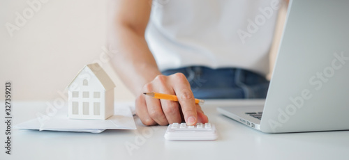 close up young man hand pressing calculator with house's model and mail letter  for check and summary expense of home loan mortgage for refinance plan and invoice monthly concept