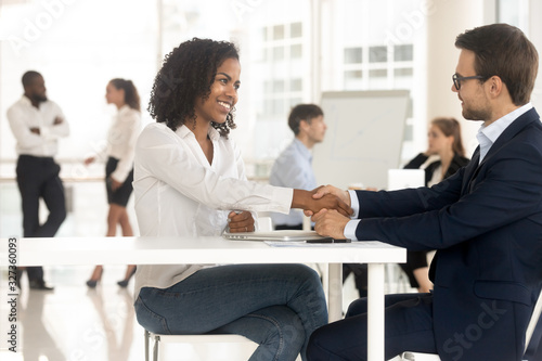 Smiling black woman handshaking with businessman for success conversation. © fizkes