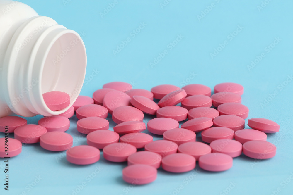 Group of pink round medicine pills and white bottle on a blue background. Selective focus. Theme of health care, medical treatment and disease prevention. Group of pink round medicine pills and white bottle on a blue background. Selective focus. Theme of health care, medical treatment and disease prevention.