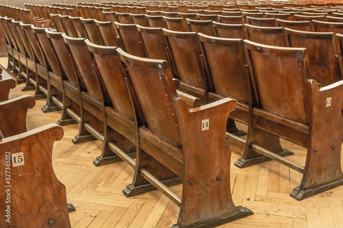 Antique wooden armchairs arranged in rows in a concert hall. Shabby surface, leather seats. Blurred image of chairs in the background.