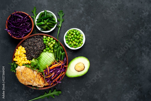 Bowl Buddha.Quinoa, chicken breast, avocado, red cabbage, arugula, carrot, green  peas, corn, broccoli, green beans in a plate on a stone background, with copy space for your text