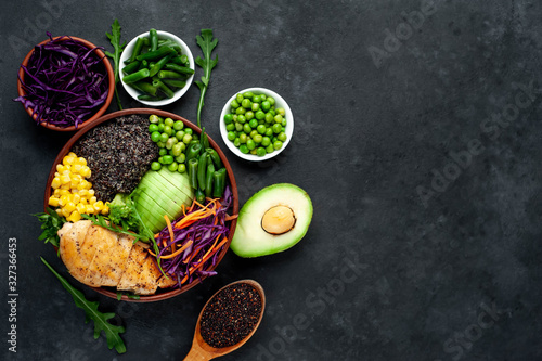 Bowl Buddha.Quinoa, chicken breast, avocado, red cabbage, arugula, carrot, green  peas, corn, broccoli, green beans in a plate on a stone background, with copy space for your text