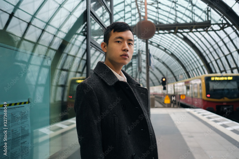 Young serious Asian businessman in coat waiting train at city subway station Young serious Asian businessman in coat waiting train at city subway station