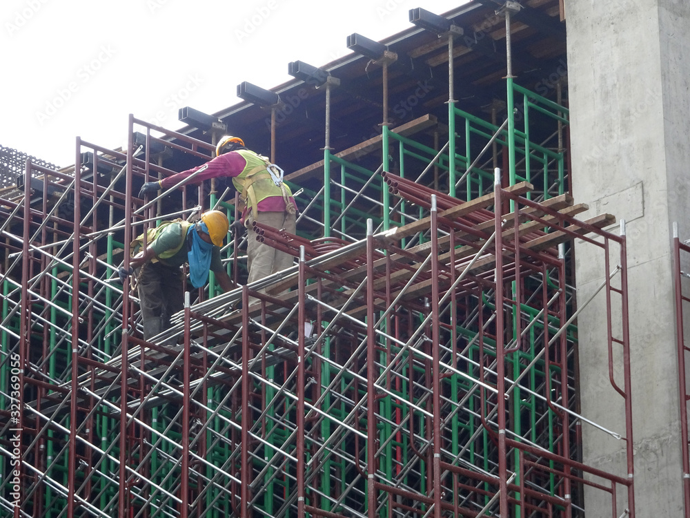 KUALA LUMPUR, MALAYSIA -JULY 28, 2019: Construction workers wearing safety gear and safety harness while installing scaffolding at a high level in the construction site.