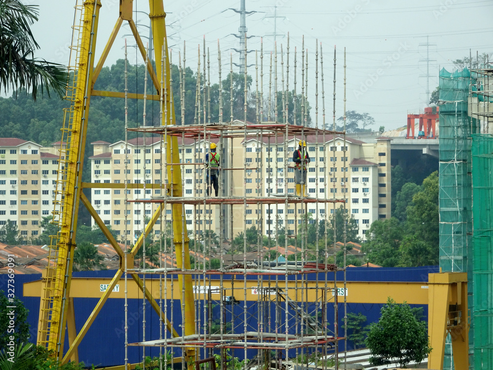 KUALA LUMPUR, MALAYSIA -JULY 28, 2019: Construction workers wearing safety gear and safety harness while installing scaffolding at a high level in the construction site.