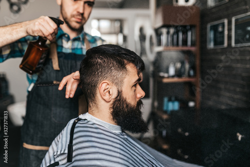 Good looking bearded man visiting hairstylist in barber shop.