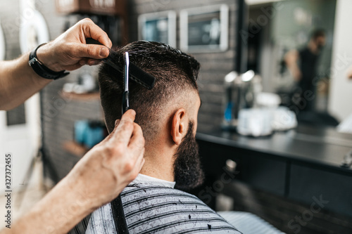 Good looking bearded man visiting hairstylist in barber shop.