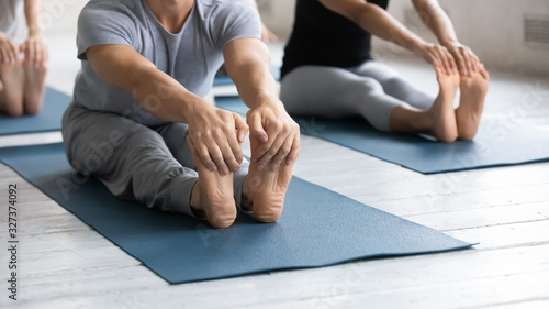 Sportive girls and guys performing Seated Forward Bend exercise