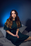 portrait of a girl in a green dress sitting on a gray bed against a blue wall