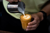 Close-up of male barista hand holding and pouring hot milk for prepare latte art on piccolo latte cup of coffee.
