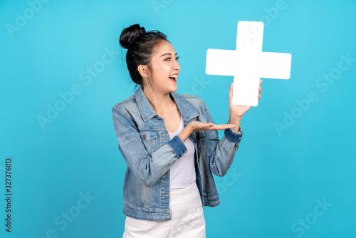 Happiness asian woman smiling, showing plus or add sign and other hand open on blue background. Cute asia girl wearing casual jeans shirt and showing join sign for increse and more benefit concept photo