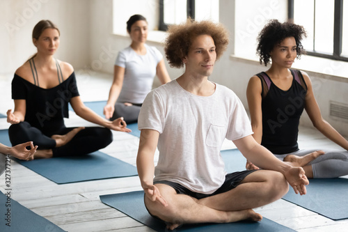 Caucasian male yogi coach and multiracial people meditating during session