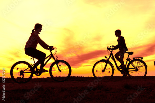 Boy and young girl riding bikes in countryside , silhouettes of riding persons at sunset in nature