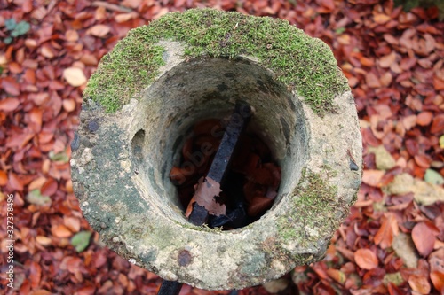 Aerial view on a stony, circular, moss covered and hollow pole with an horizontal withered metal stick in it in an autumn scenery