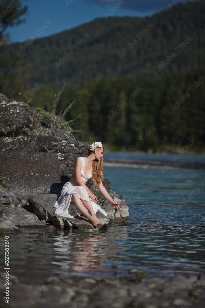 A girl in white clothes stands on a rocky shore near the river. A girl in white clothes stands on a rocky shore near the river.