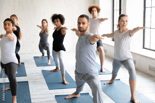 Seven multiethnic people beginners practicing yoga performing Warrior II pose