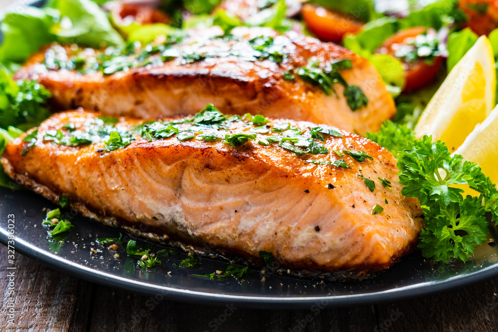 Fried salmon steaks with vegetables on wooden table Fried salmon steaks with vegetables on wooden table