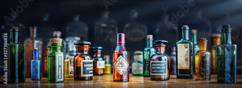 A bottle of poison on a background of old medical, chemistry and pharmacy glass. Chemistry and pharmacy history panoramic concept background. Retro style.