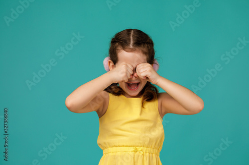 upset little child girl is crying on blue background. girl wiping tears