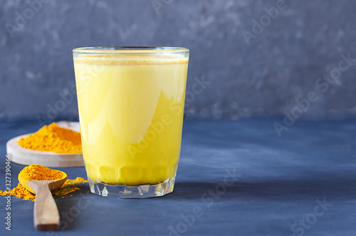 Healthy golden milk with turmeric and honey on a blue background and tiextile. Diet, vegan and detox hot drink. Trendy drink. Copy space. Flat lay.