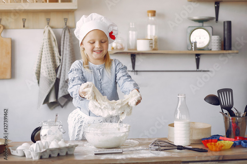 Child in a kitchen. Little girl with a dough. Kid in a blue shirt and white shef hat