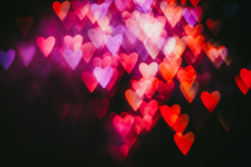 Bokeh hearts. Valentine day party. Pink red defocused glow on black background.