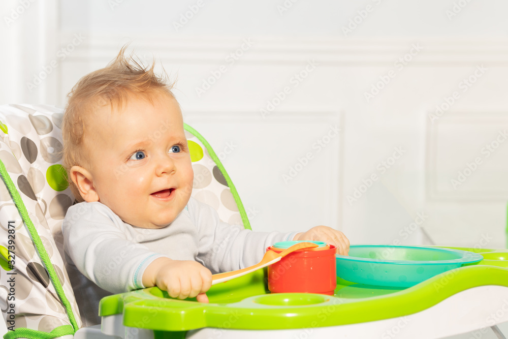 Happy little toddler baby boy sit in highchair holding plastic spoon and smiling Happy little toddler baby boy sit in highchair holding plastic spoon and smiling