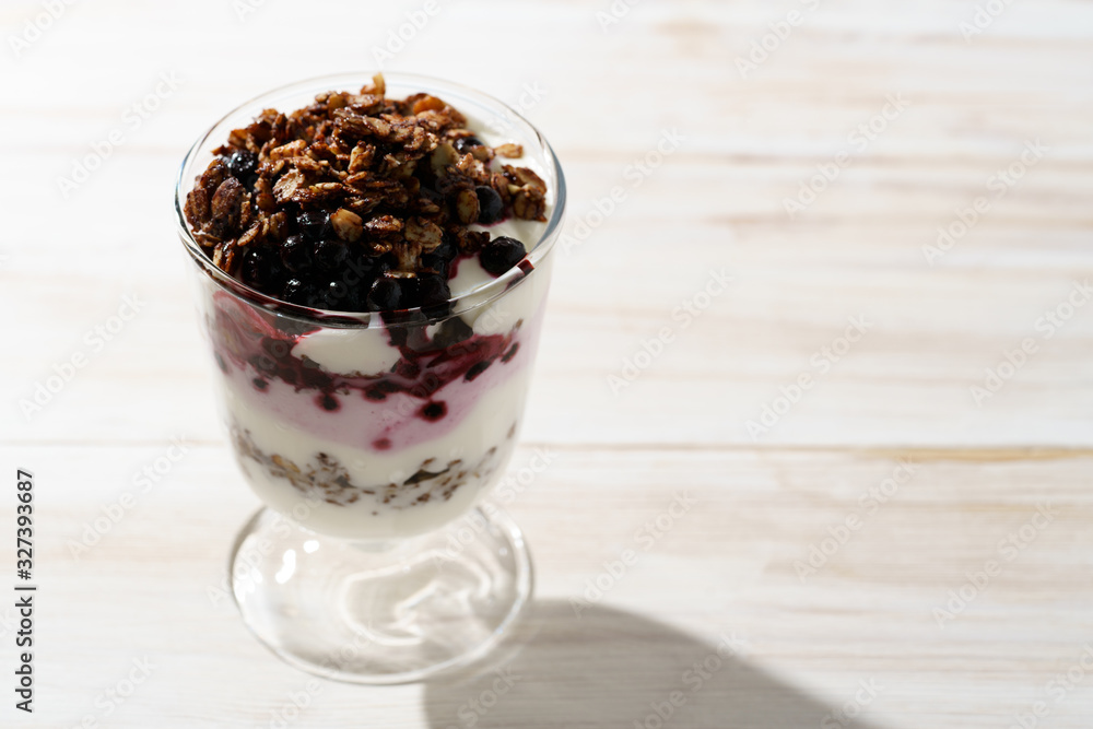 Yogurt parfait with cocoa granola and frozen blueberries. White wooden table, hard light, high resolution Yogurt parfait with cocoa granola and frozen blueberries. White wooden table, hard light, high resolution