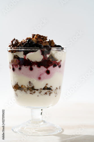Yogurt parfait with cocoa granola and frozen blueberries. White wooden table, hard light, high resolution