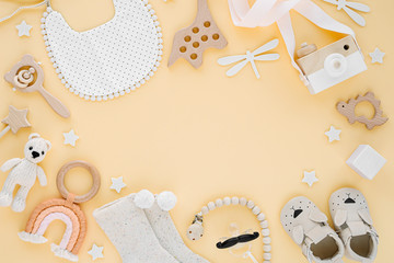 Toys, bib, socks, slippers for newborn on yellow background.  Frame made of  gender neutral baby stuff and accessories. Flat lay, top view