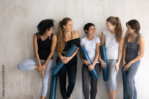Five diverse cheerful girls holding yoga mats chatting after workout