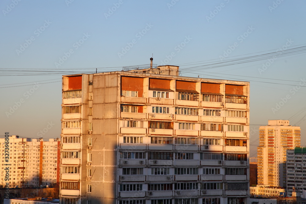 Top storeys of high-rise Soviet residential building with strung wires in the Moscow district of Konkovo on a winter evening with sun rays and shadows