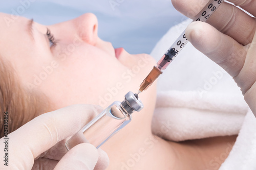 hands in gloves are gaining an injection from a jar into a syringe on the background of the girl's face photo