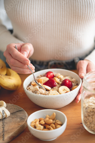 Woman eating oatmeal porridge with fruits. Concept of healthy lifestyle and dieting. Warm morning light, healthy breakfast on wooden table